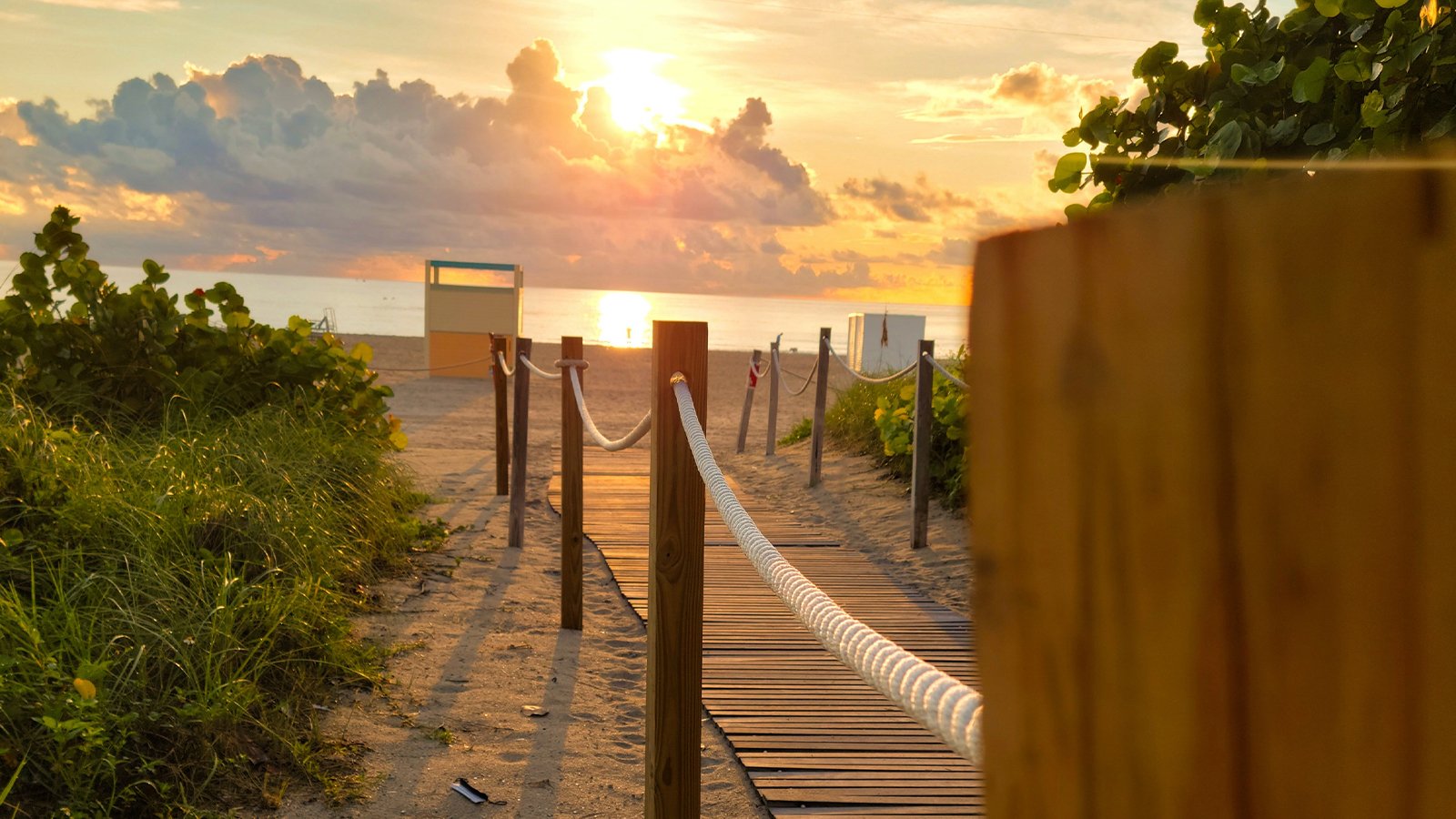 A boardwalk leading out to Miami Beach with the sun rising in the background.