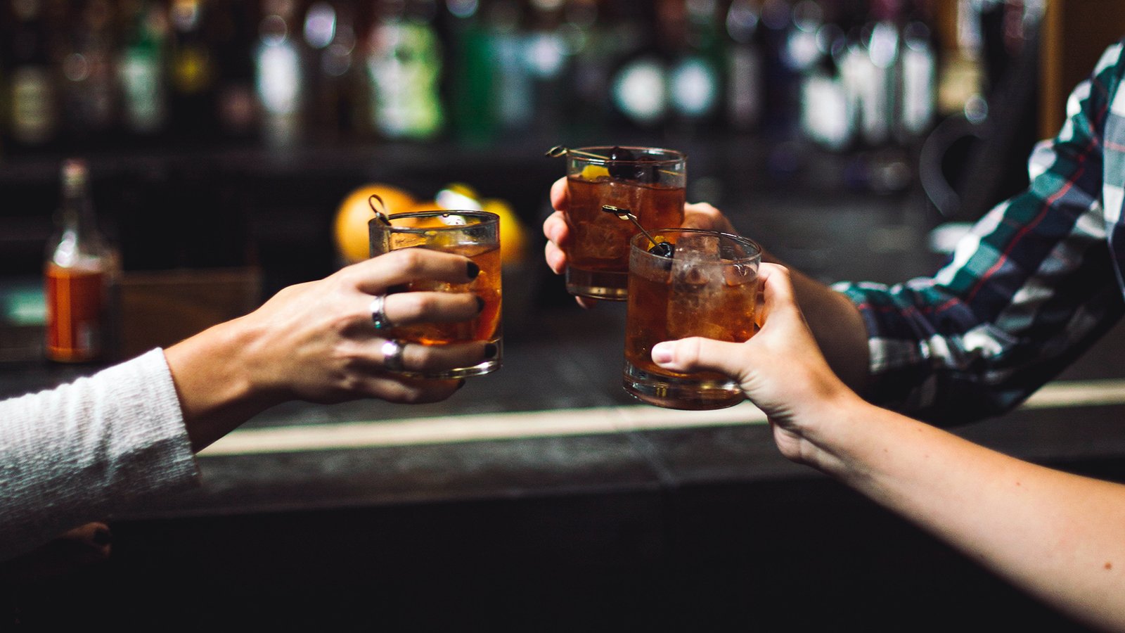 Three people holding drinks at a bar in Nashville.