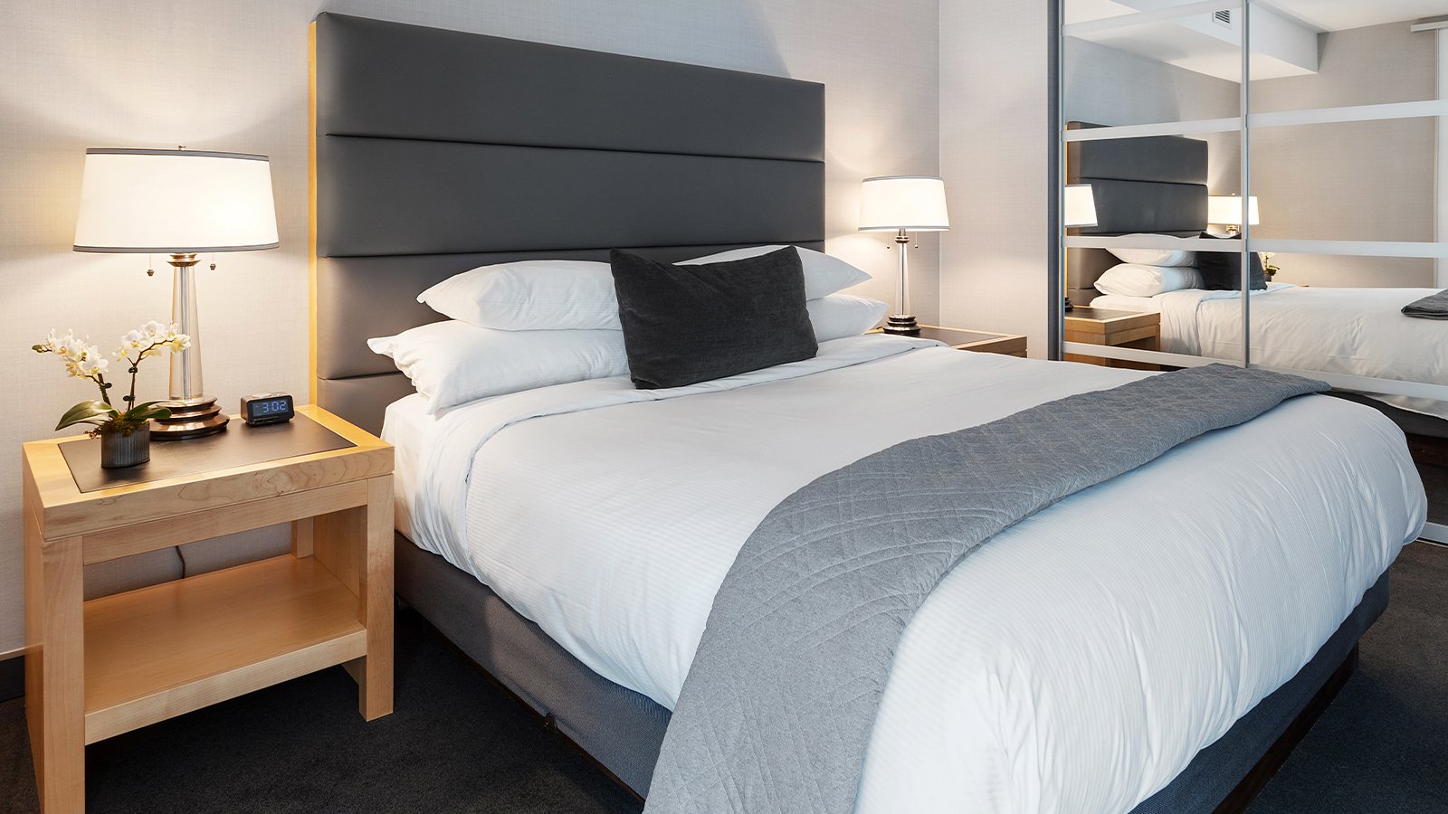 A hotel room with the bed made and lamps on.