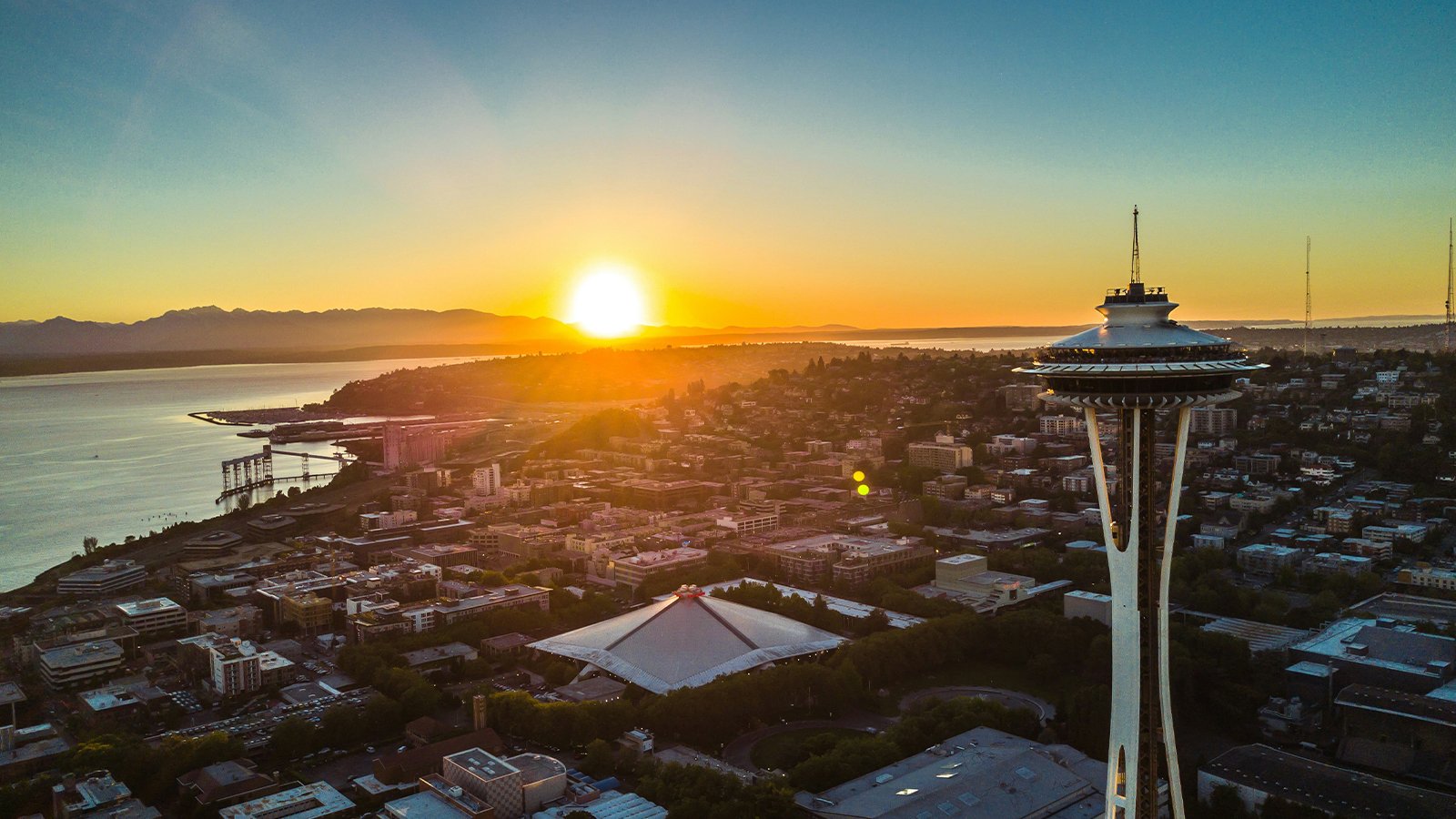 A view of the Seattle Space Needle with the sun setting in the distant background.