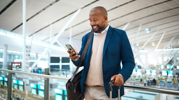 Happy businessman checking travel information on mobile app while standing in an airport.