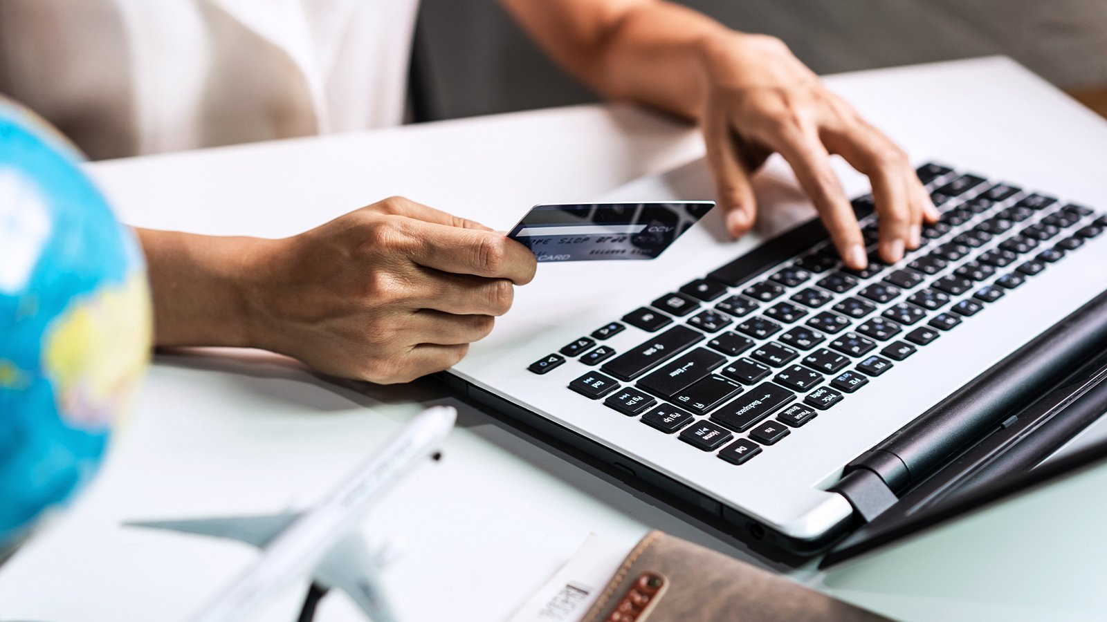 Closeup of a person holding their credit card while booking their next business trip on a laptop.