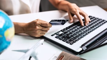 Closeup of a person holding their credit card while booking their next business trip on a laptop.
