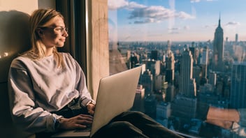 Young business traveler with laptop technology sitting at panoramic windowsill and enjoying beautiful view of Manhattan