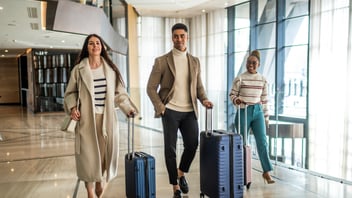 Three young colleagues seen walking from the elevator with their luggage, just after they checked in at the reception desk in the hotel where they will be staying for a few days for business