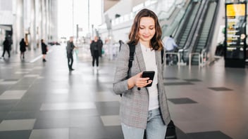 Young female business traveler looking at her smartphone while walking through an airport.