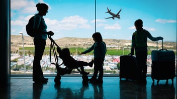 Mother with kids and luggage looking at planes in airport while on a family business travel trip