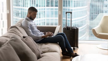A businessman sitting on a couch working on his laptop in a luxury business hotel.