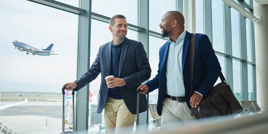 Two co-workers walking through an airport together with a plane taking off in the background.