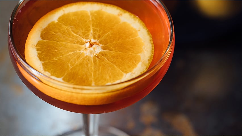 Close-up of an orange cocktail garnished with a fresh orange slice in a coupe glass.