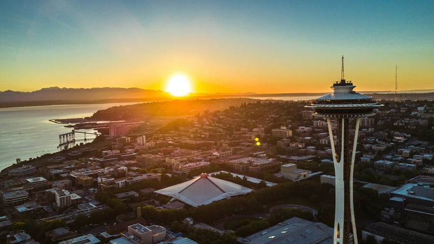 A view of the Seattle Space Needle with the sun setting in the distant background.