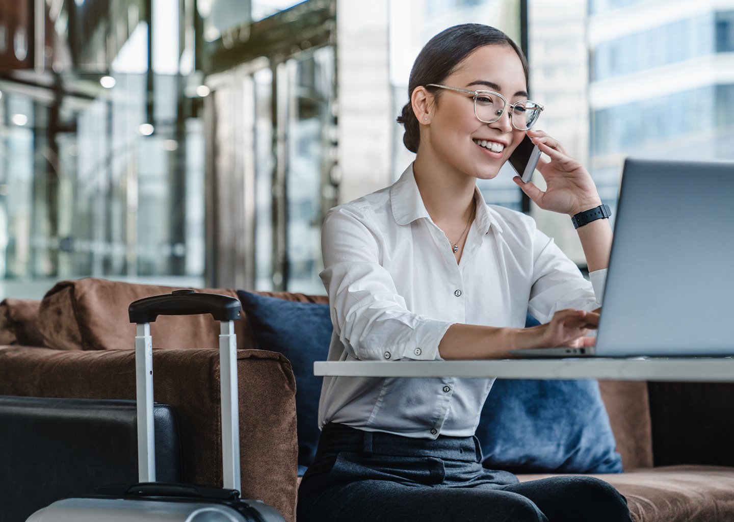 Asian female sitting at airport before trip having phone conversation with client.