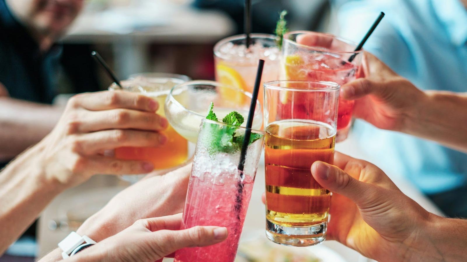 Several hands toasting with different cocktails