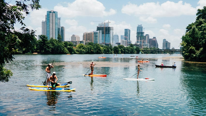 People paddleboarding on Lady Bird Lake with Austin's downtown skyline in the background.