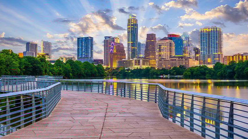 Austin skyline at sunset viewed from a waterfront boardwalk with metal railings.