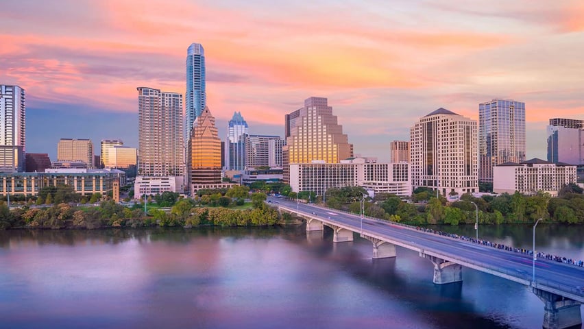 Austin downtown skyline at dusk with a bridge crossing Lady Bird Lake in soft light.