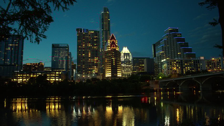 Austin city skyline illuminated at night with lights reflecting on the water below.