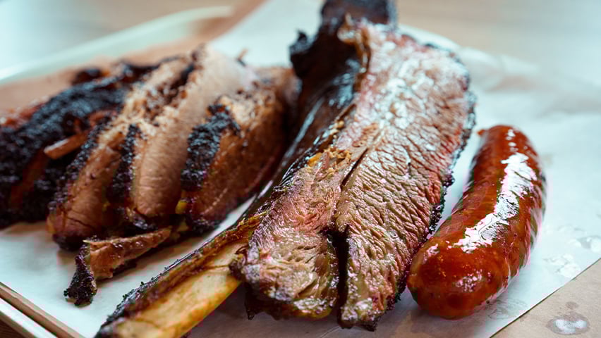 Sliced Texas barbecue brisket and sausage on butcher paper, showing the meat's smoky bark.
