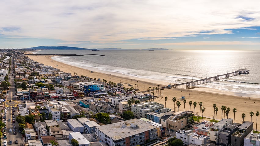 Aerial view of coastal California beach town with pier extending into the Pacific Ocean.