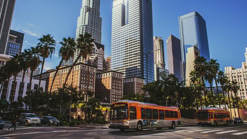 Orange Metro bus driving through downtown Los Angeles with modern skyscrapers and palm trees.