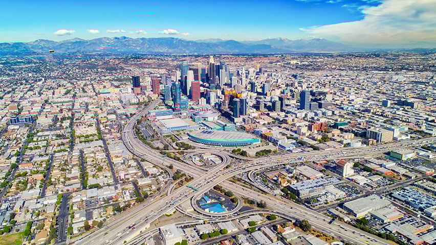Aerial panoramic view of downtown Los Angeles with freeway interchanges and surrounding cityscape.