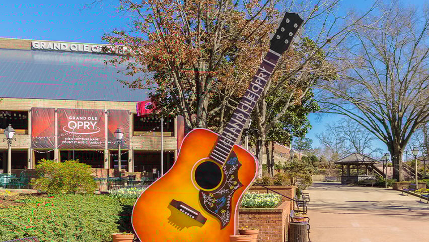 Giant acoustic guitar sculpture outside the Grand Ole Opry building in Nashville with autumn trees and blue sky.