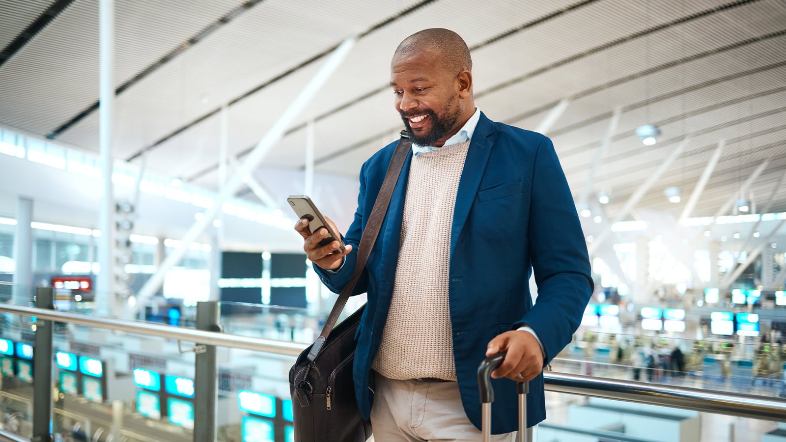 Happy businessman checking travel information on mobile app while standing in an airport.