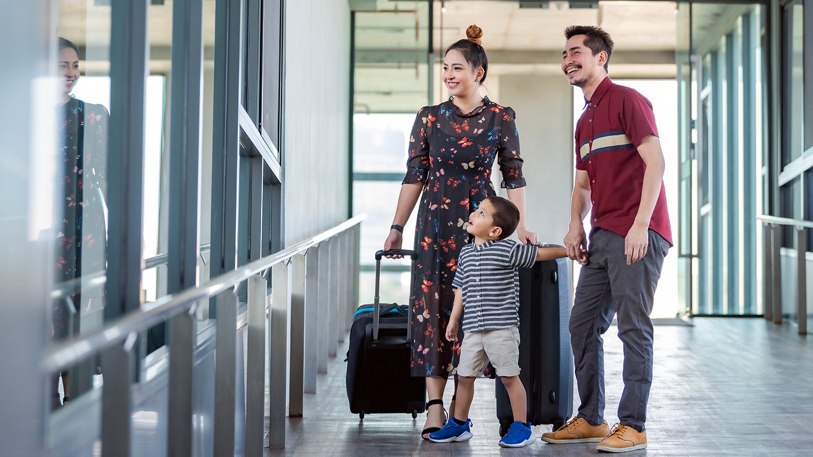 Happy young family of three walking with suitcases at airport terminal