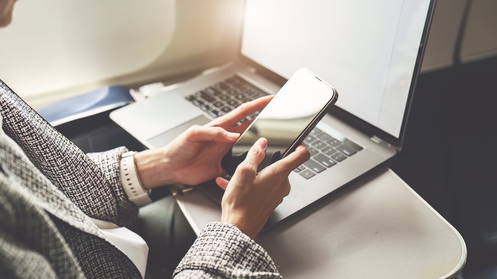 A businesswoman in formal suit using a smartphone and laptop during flight