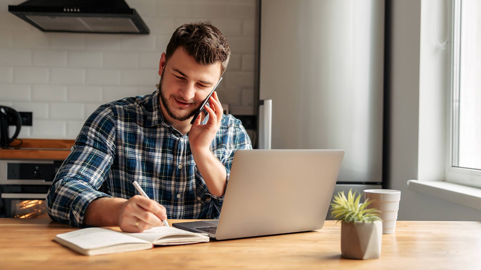 Young man works on laptop in home kitchen